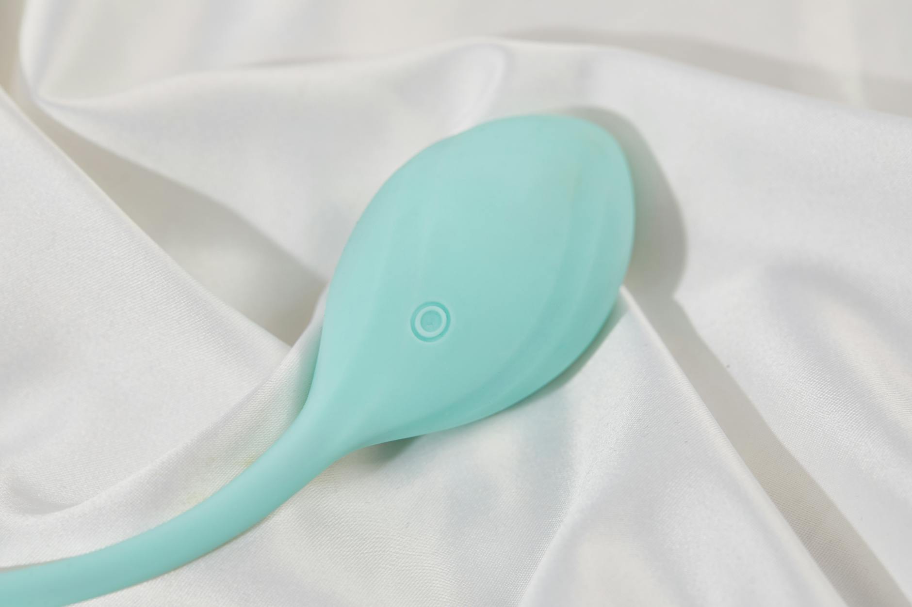 Sleek teal clitoral vibrator resting on white silk fabric