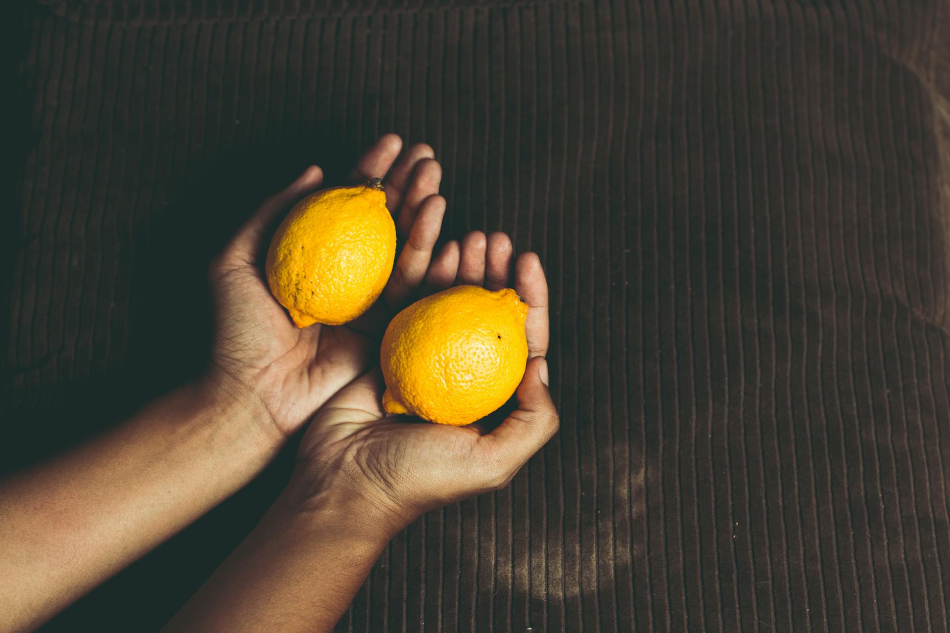 Close-up of two fresh lemons held in cupped hands on a brown surface, symbolizing freshness and renewal across time.