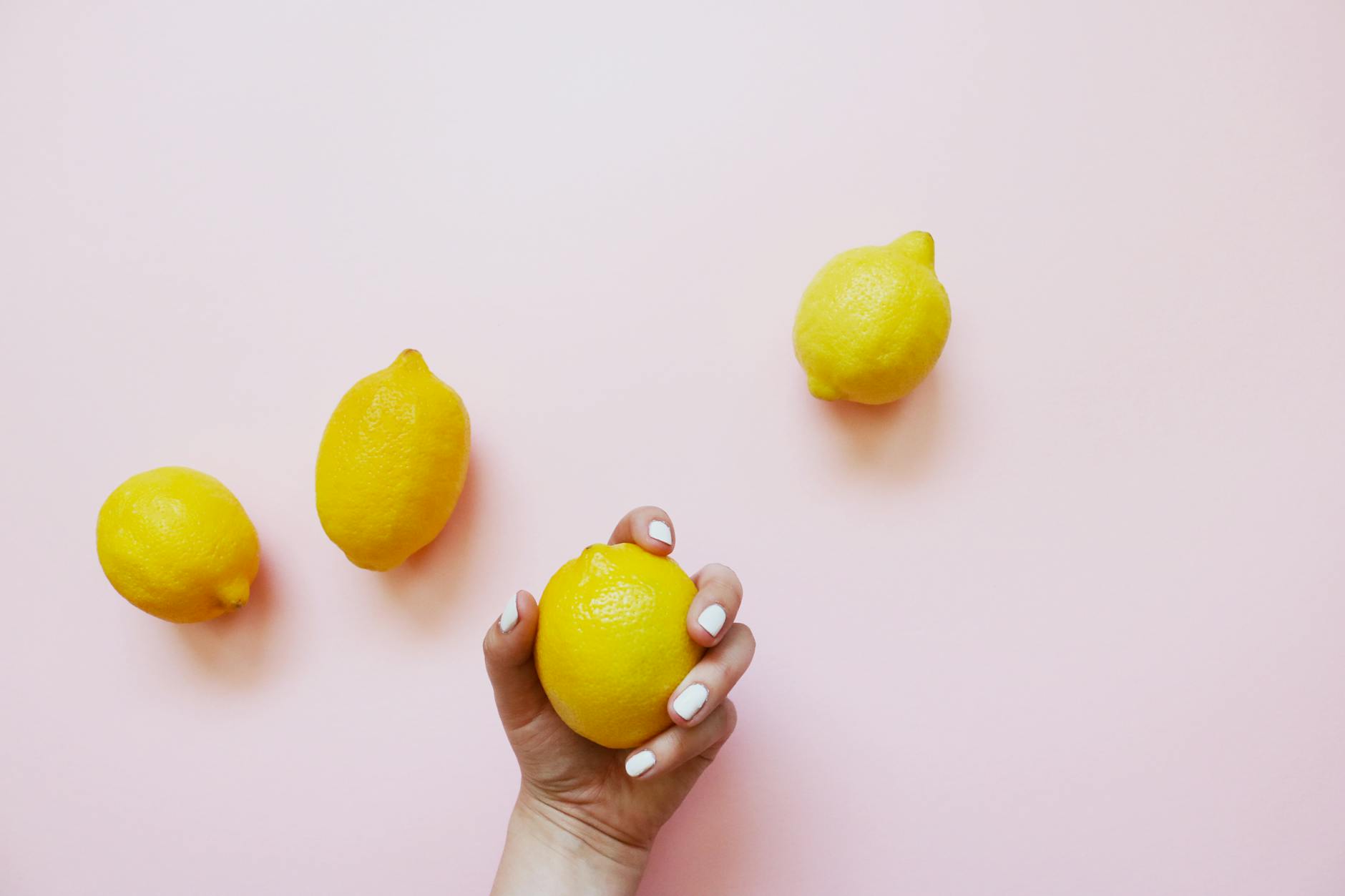 A hand holding a fresh lemon on a soft pink background, symbolizing intimate self-care and desire