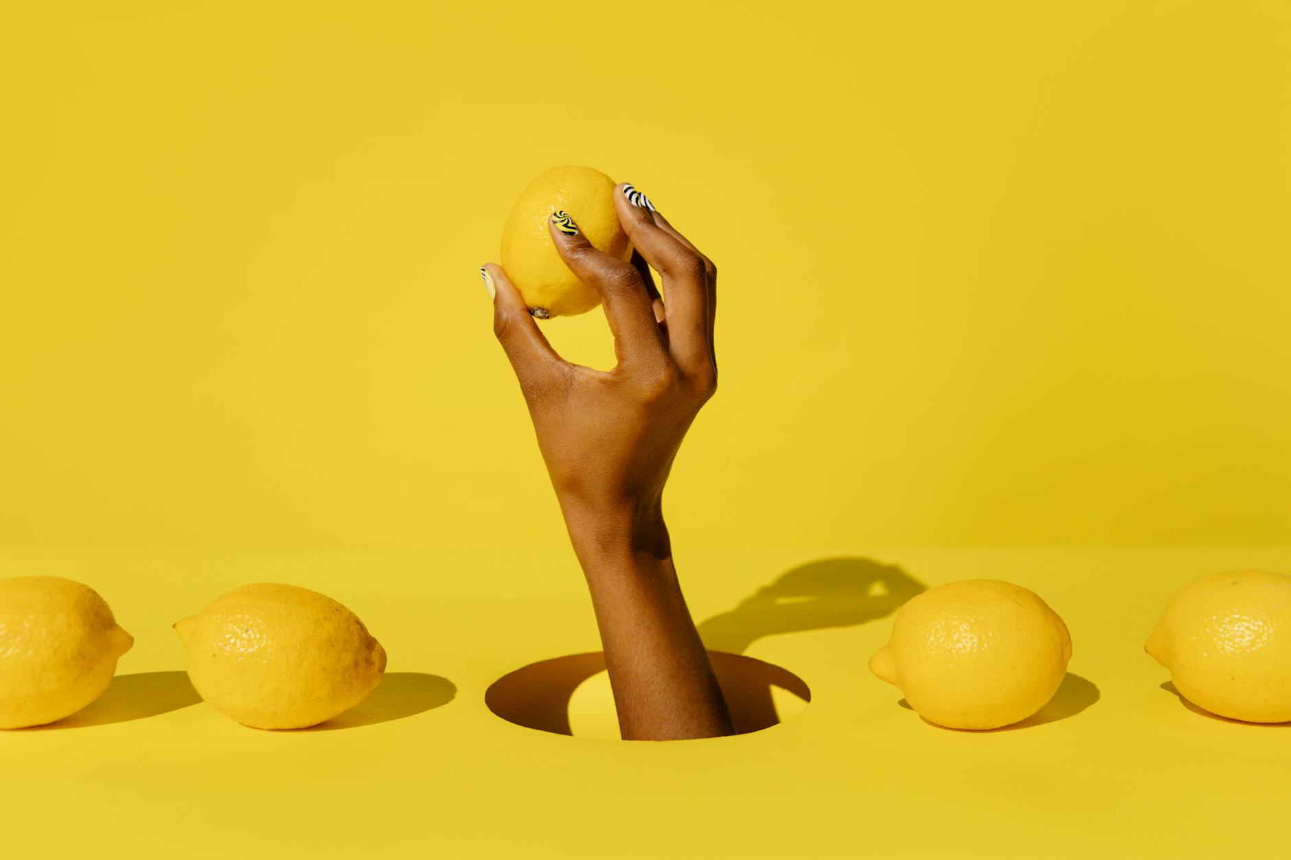 A hand holding a fresh lemon against a bright yellow background, symbolizing the vibrant intensity of lemon vibrators.
