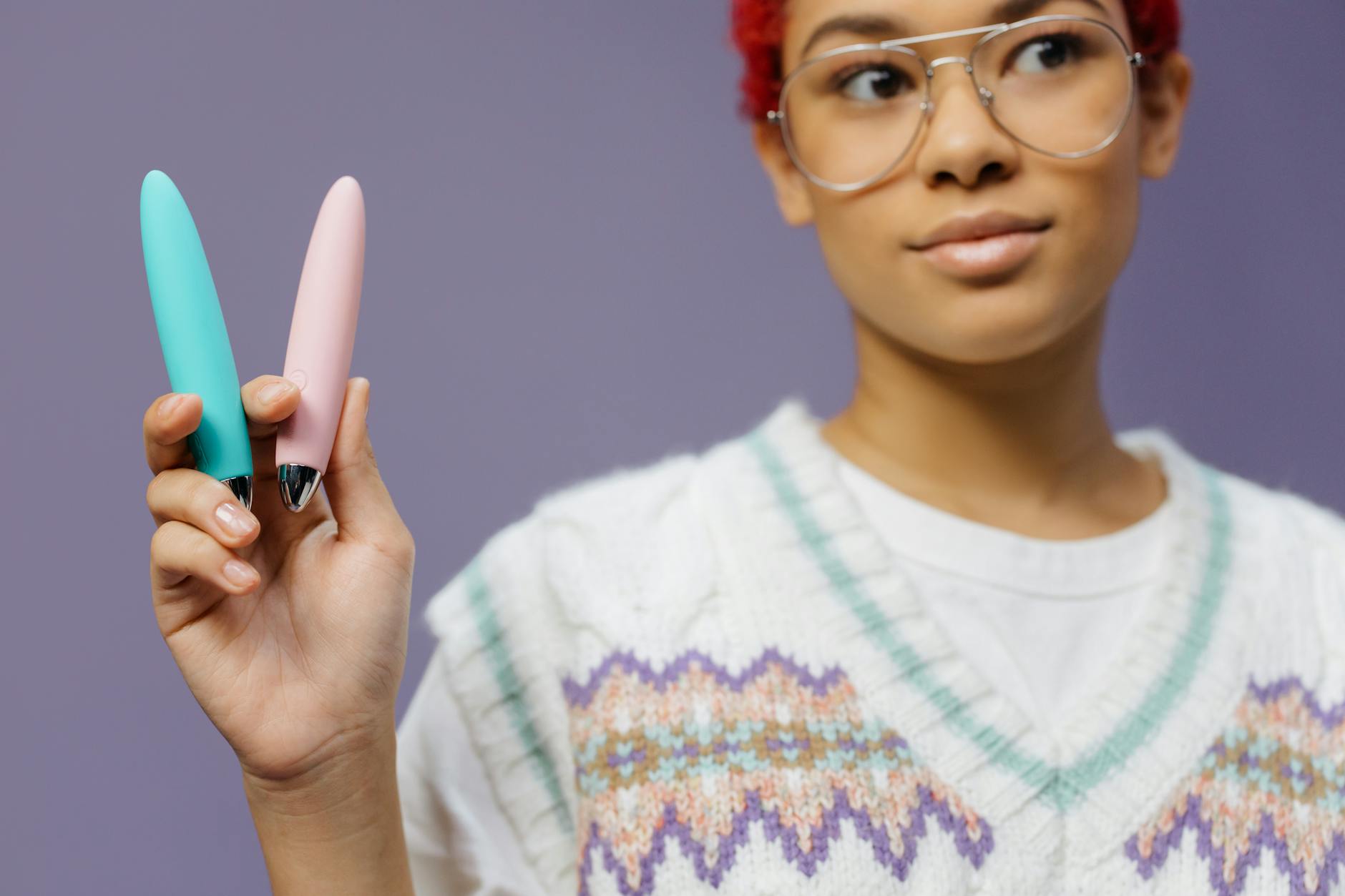 Hand holding a blue silicone vibrator against a purple background
