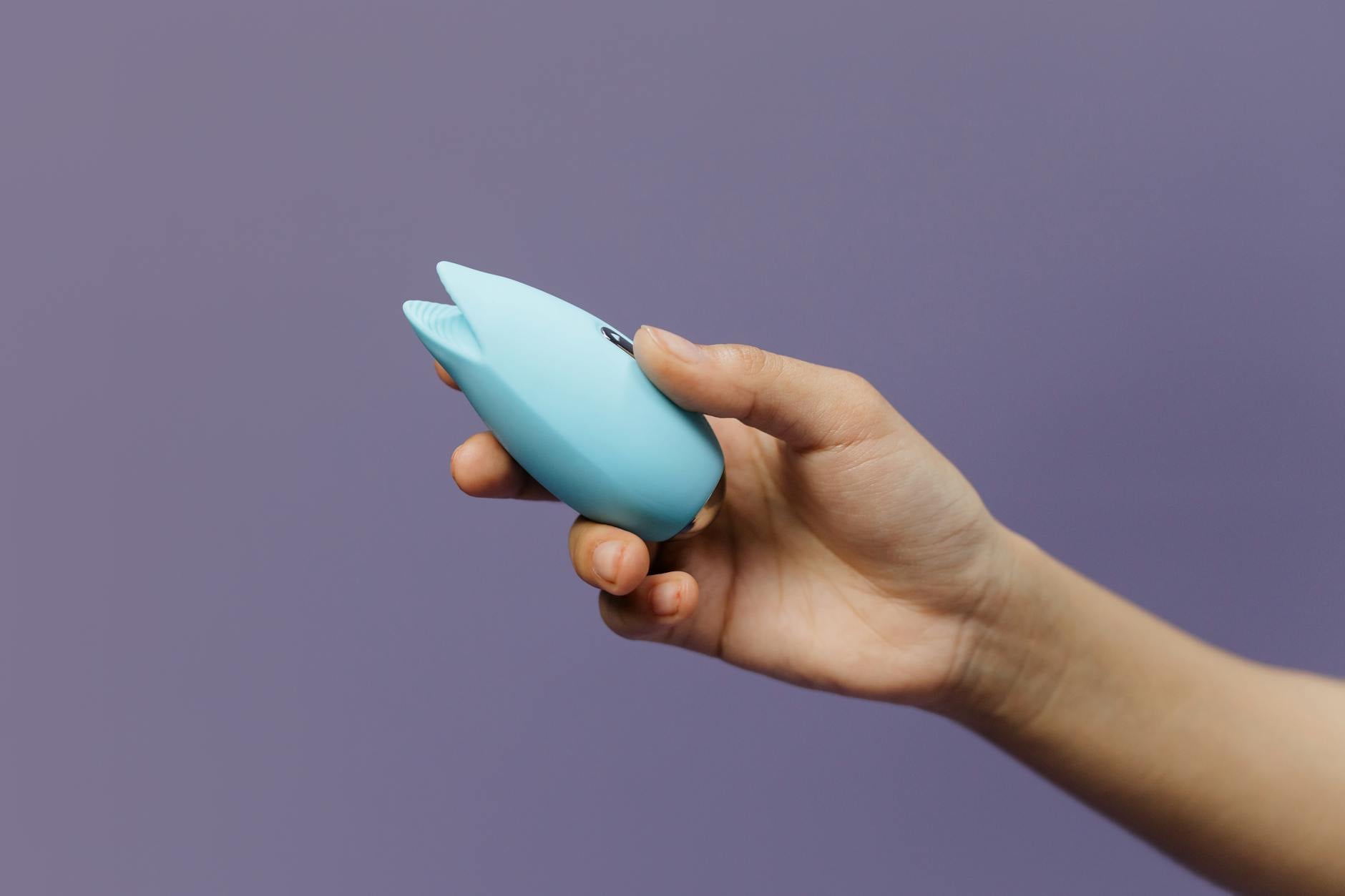 Two hands holding vibrators against a pastel background during intimate moments