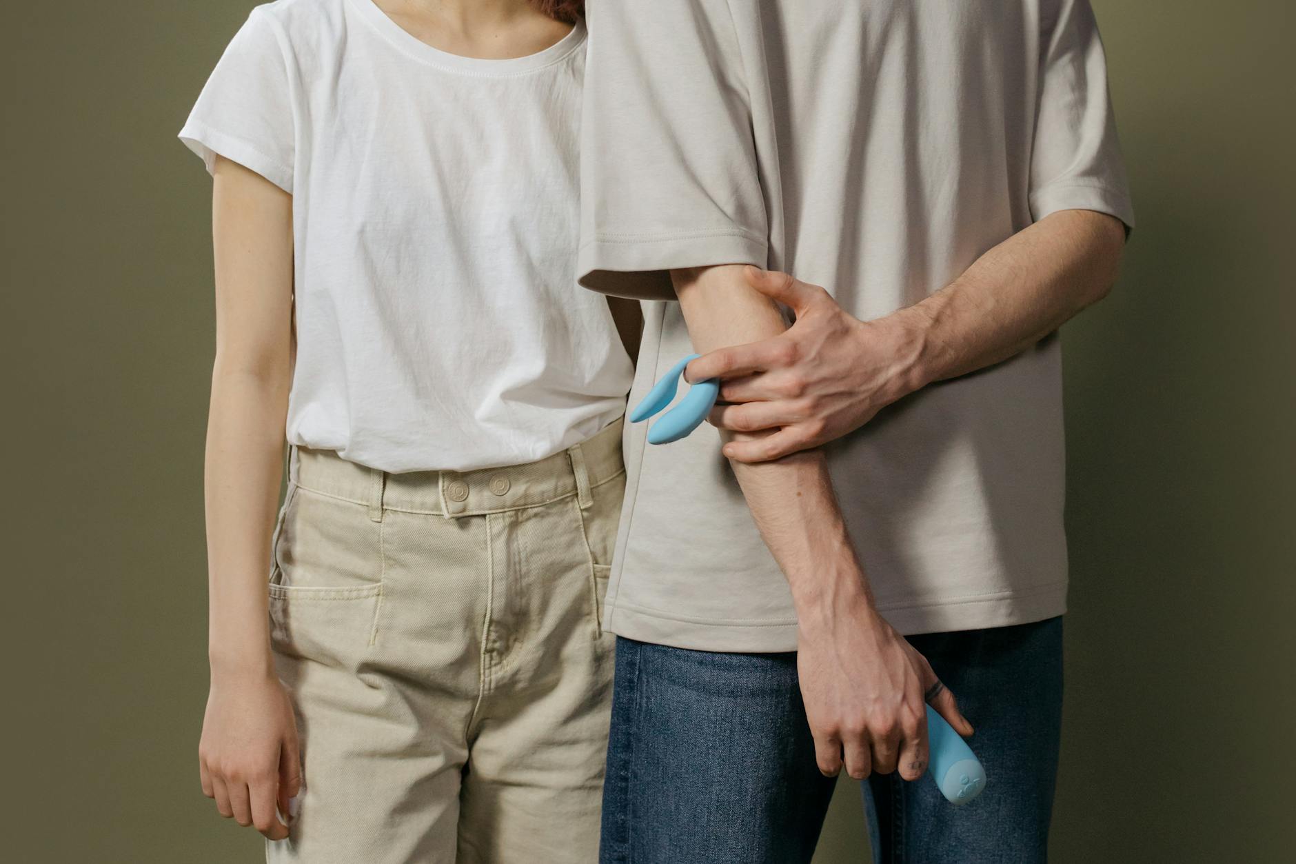 A young couple standing together indoors, holding a blue vibrator, symbolizing modern intimacy and shared exploration.